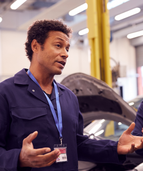 A worker in an autoshop appears to be instructing others in front of a car being repaired.