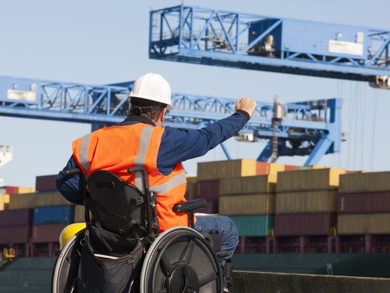 Transportation engineer worker and wheelchair user giving directions to shipping containers at a shipping port.