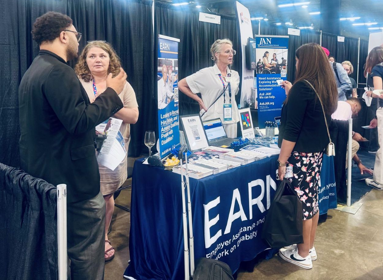 Attendees speak with EARN staff at the EARN exhibit booth at the Disability:IN 2026 Global Conference and Expo. The booth includes signage for EARN and the Job Accommodation Network alongside informational materials.