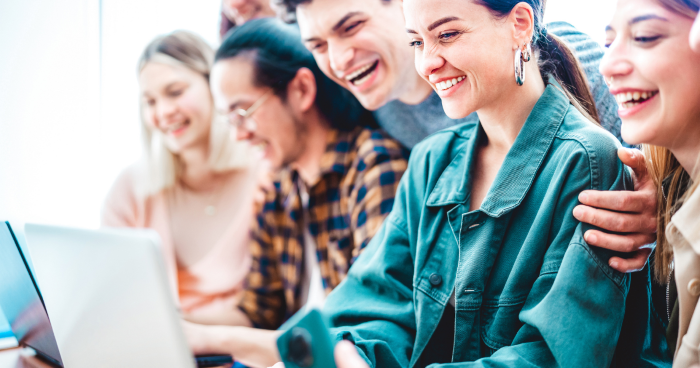 A group of young professionals looking at laptops together while smiling and laughing