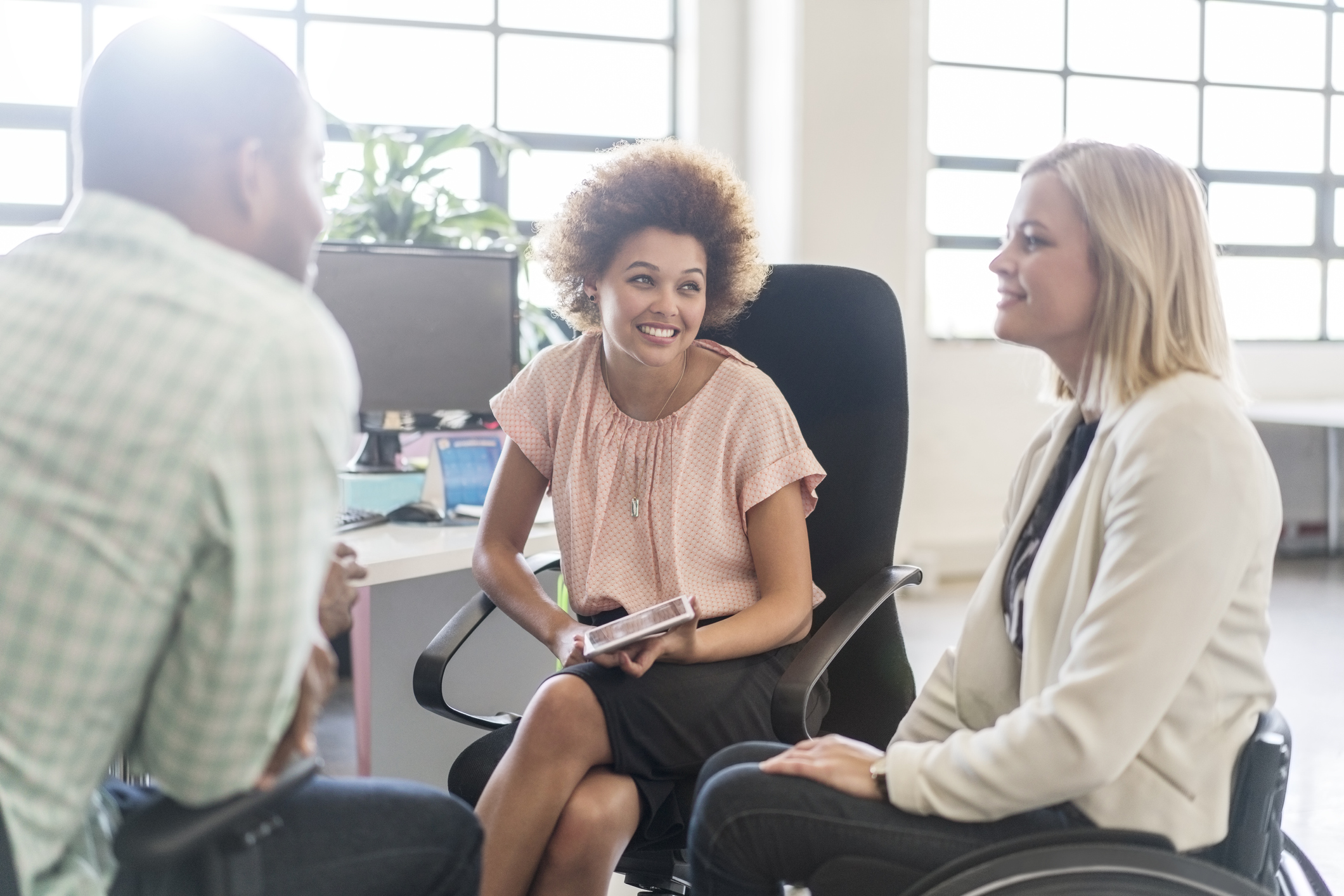 Three smiling people sit in a circle in an office setting, actively listening to one another