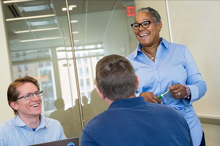 A smiling woman address two colleagues