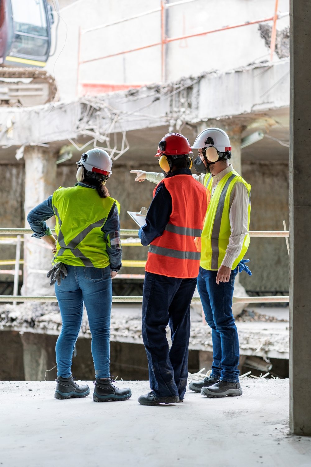 A group of construction workers wearing safety vests, ear protection, and hard hats on a job site