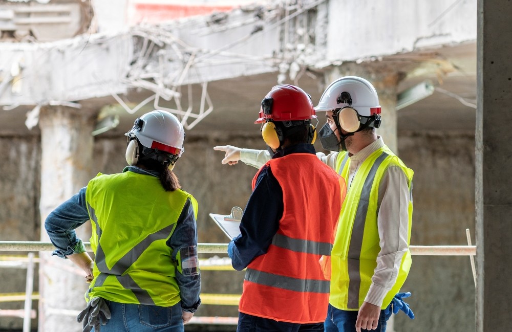 A group of construction workers wearing safety vests, ear protection, and hard hats on a job site