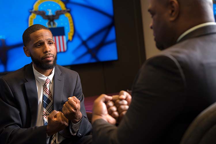 Two men sign to each other against a federal government symbol