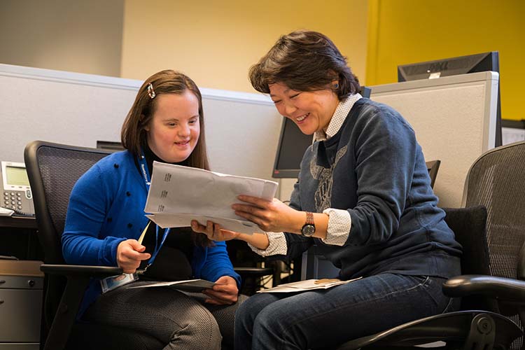 A woman assists a young woman with Down's Syndrome.