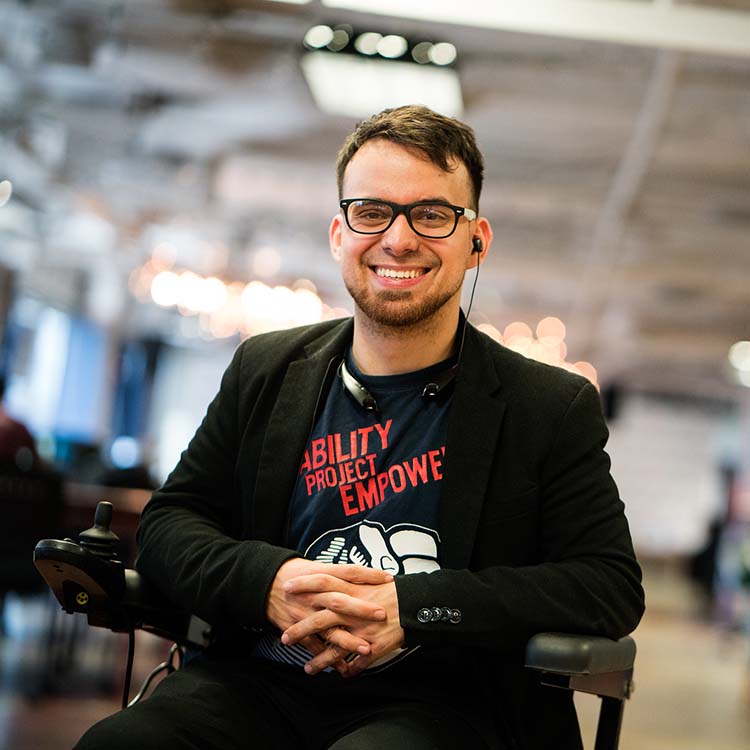 A smiling man with an earpiece sits in a wheelchair