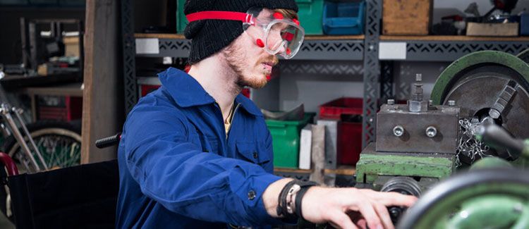 A man in goggles sits in a wheelchair and operates machinery