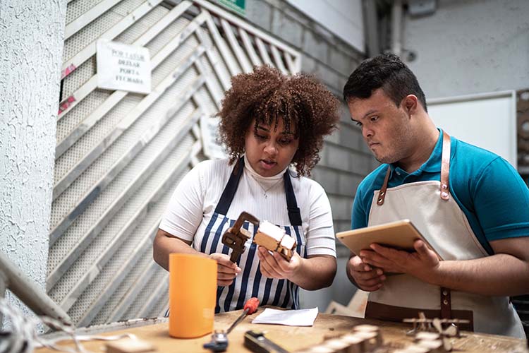 Image of a woman illustrating how to perform a task to a man with down's syndrome.