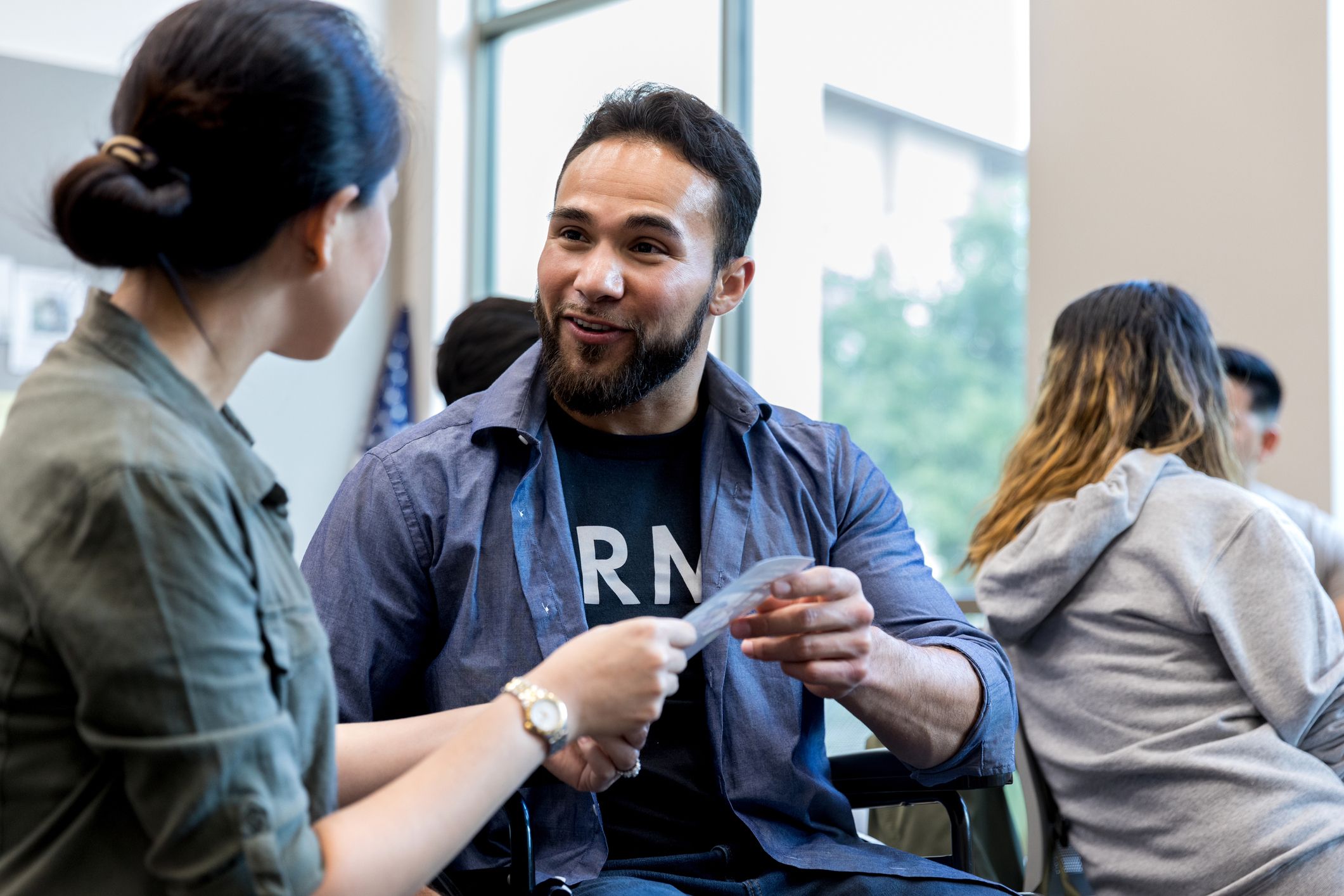 Veteran in an army t-shirt receives a brochure from another person. Other small groups meet in the background.