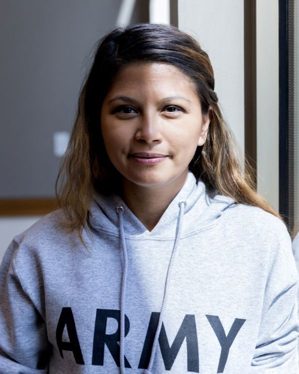 Portait of a veteran wearing a hooded sweatshirt that reads "army," sitting against a classroom window