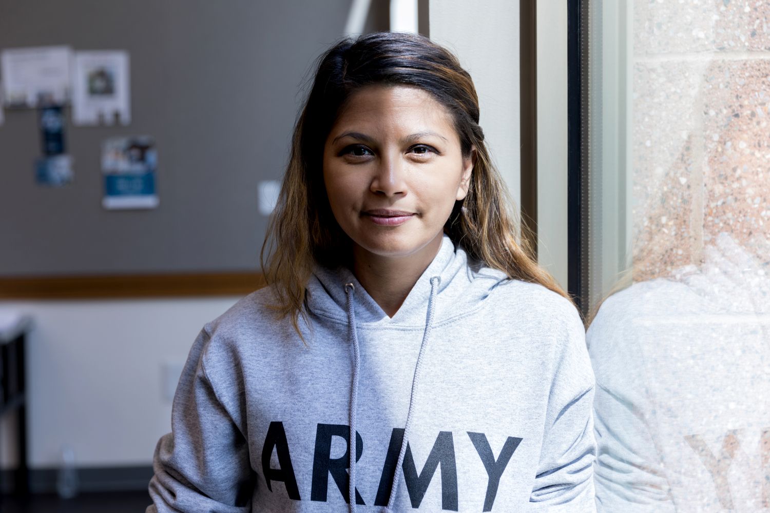 Portait of a veteran wearing a hooded sweatshirt that reads "army," sitting against a classroom window
