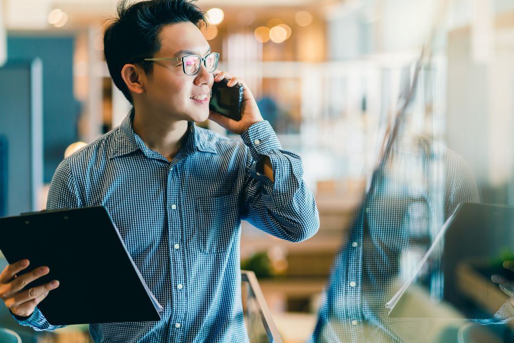 A young professional walking up stairs while holding a clipboard and talking on their phone